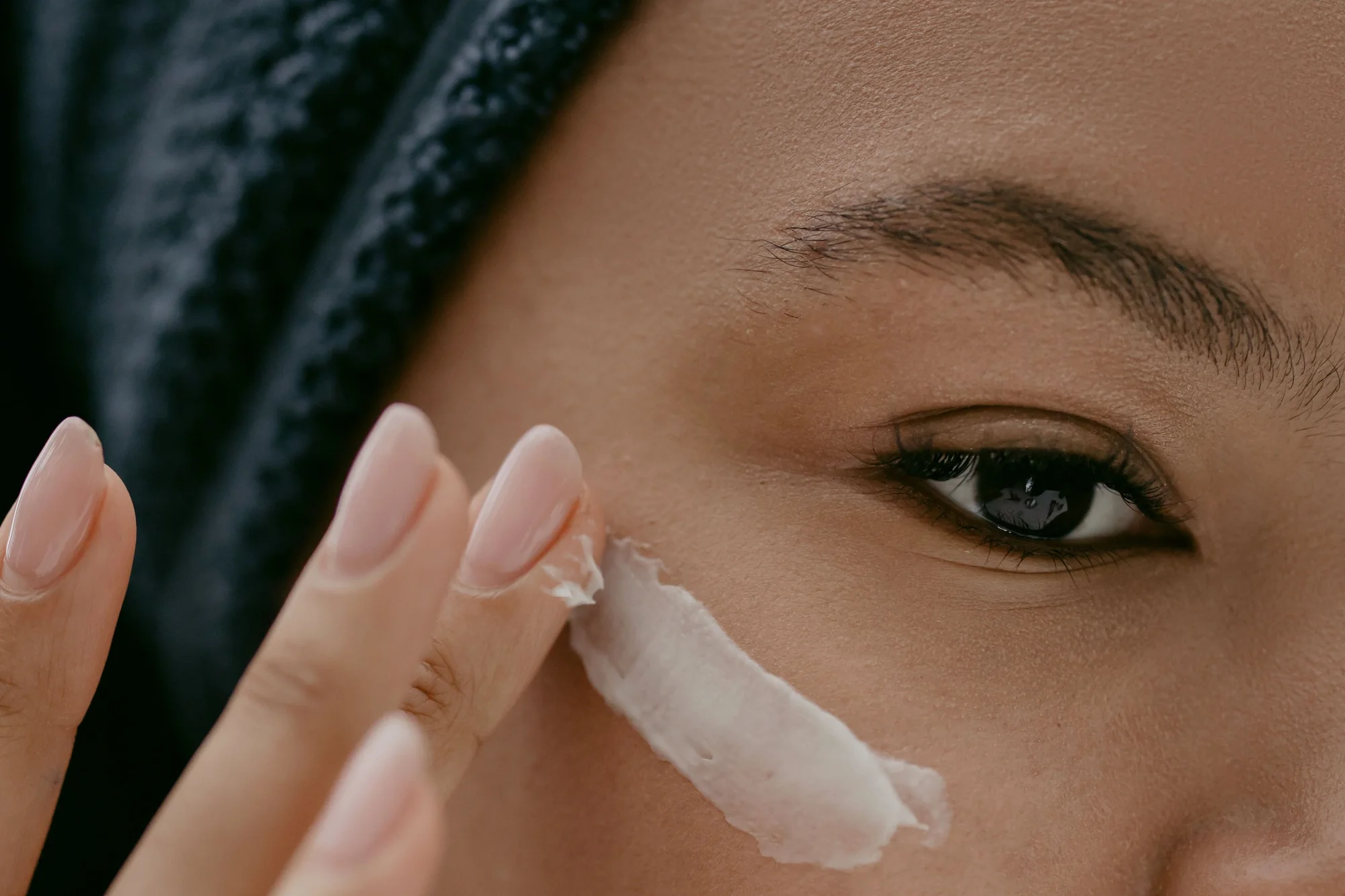Primer plano de una mujer que aplica crema hidratante en la piel debajo del ojo