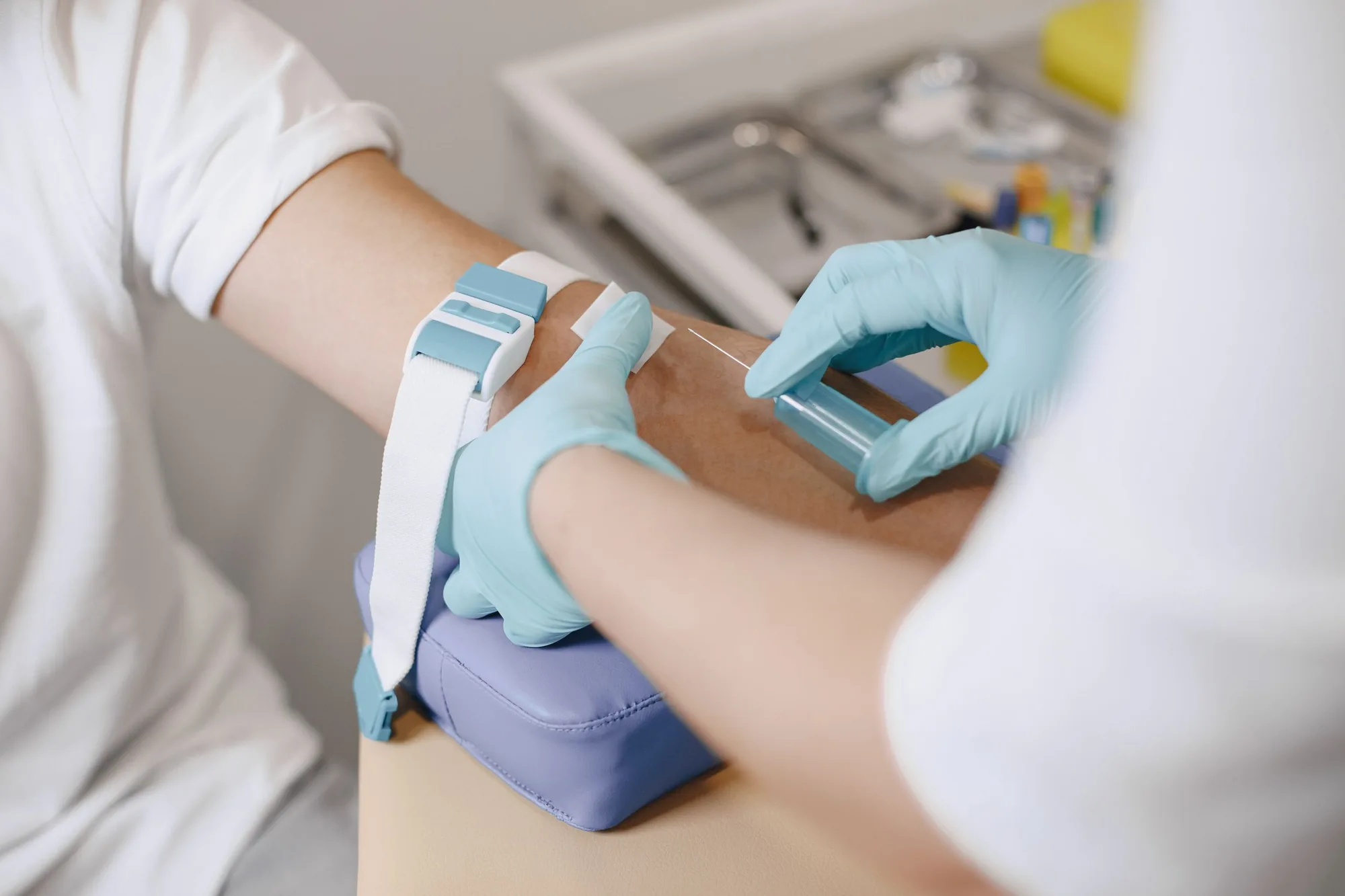 Brazo con torniquete mientras unas manos con guantes preparan la extracción de sangre para el plasma